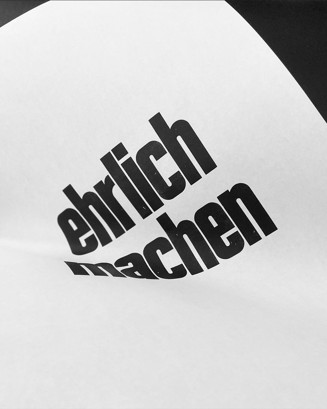 Detailaufnahme des handgesetzten Bleisatz-Druckes mit den Worten »ehrlich machen« in schwarzer Groteskschrift auf Dünndruckpapier, ungerahmt und gewölbt auf schwarzem Hintergrund