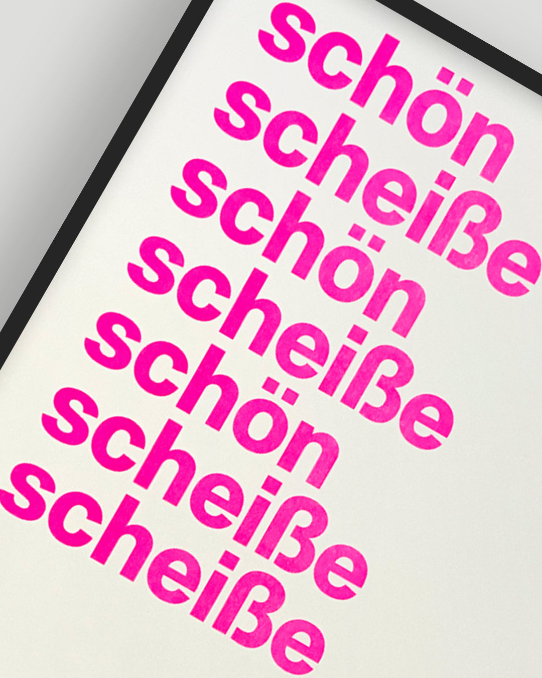 Nahaufnahme eines RISO-Druckes mit den Worten »schön« und »scheiße« in pinker Groteskschrift auf cremefarbenen Papier, gerahmt mit schwarzem Rahmen vor hellgrauem Hintergrund, nummeriert und signiert