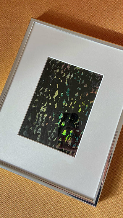 Mehrfarbige Chirografie in Acryl und Kreide auf Karton, gerahmt mit Passepartout und Aluminiumrahmen, liegend auf gelbem Polster
