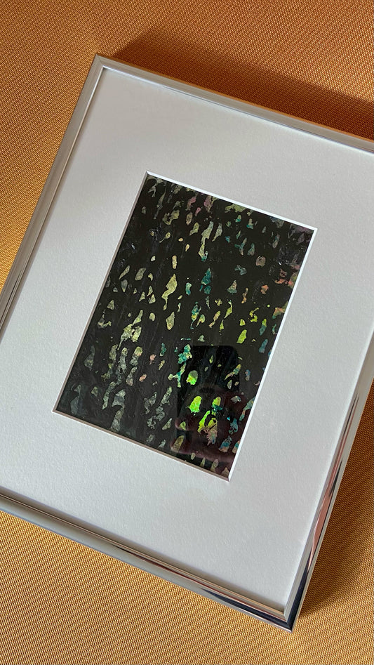 Mehrfarbige Chirografie in Acryl und Kreide auf Karton, gerahmt mit Passepartout und Aluminiumrahmen, liegend auf gelbem Polster
