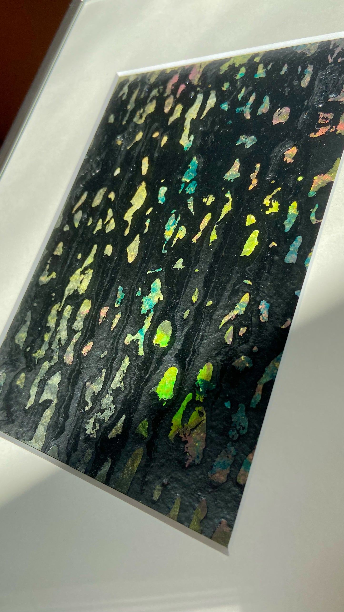 Nahaufnahme einer mehrfarbigen Chirografie in Acryl und Kreide auf Karton, gerahmt mit Passepartout und Aluminiumrahmen, partiell mit Sonnenlicht beleuchtet