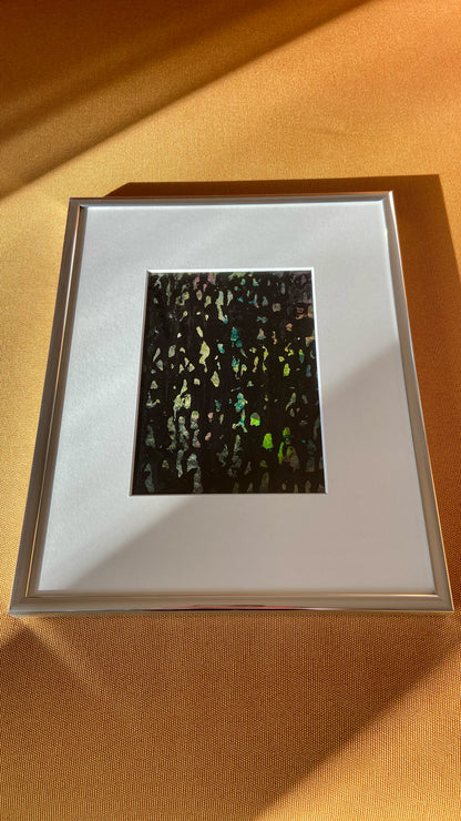 Mehrfarbige Chirografie in Acryl und Kreide auf Karton, gerahmt mit Passepartout und Aluminiumrahmen, liegend auf gelbem Polster, partiell mit Sonnenlicht beleuchtet