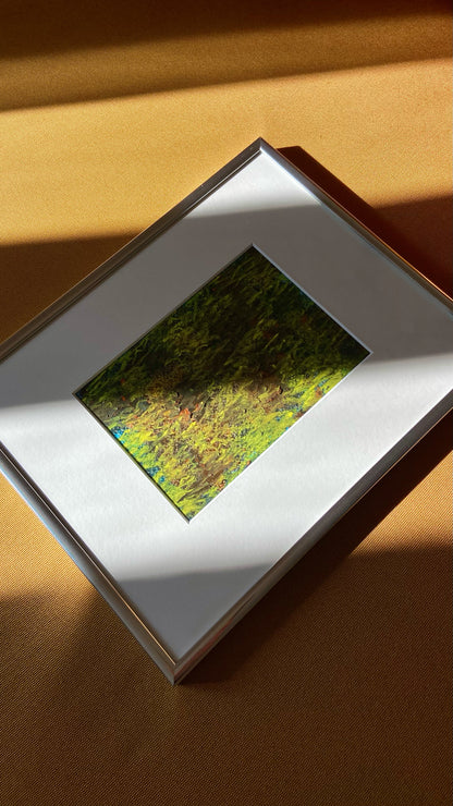 Mehrfarbige Chirografie in Kreide und Ölpastell auf Karton, gerahmt mit Passepartout und Aluminiumrahmen, liegend auf gelbem Polster, partiell mit Sonnenlicht beleuchtet