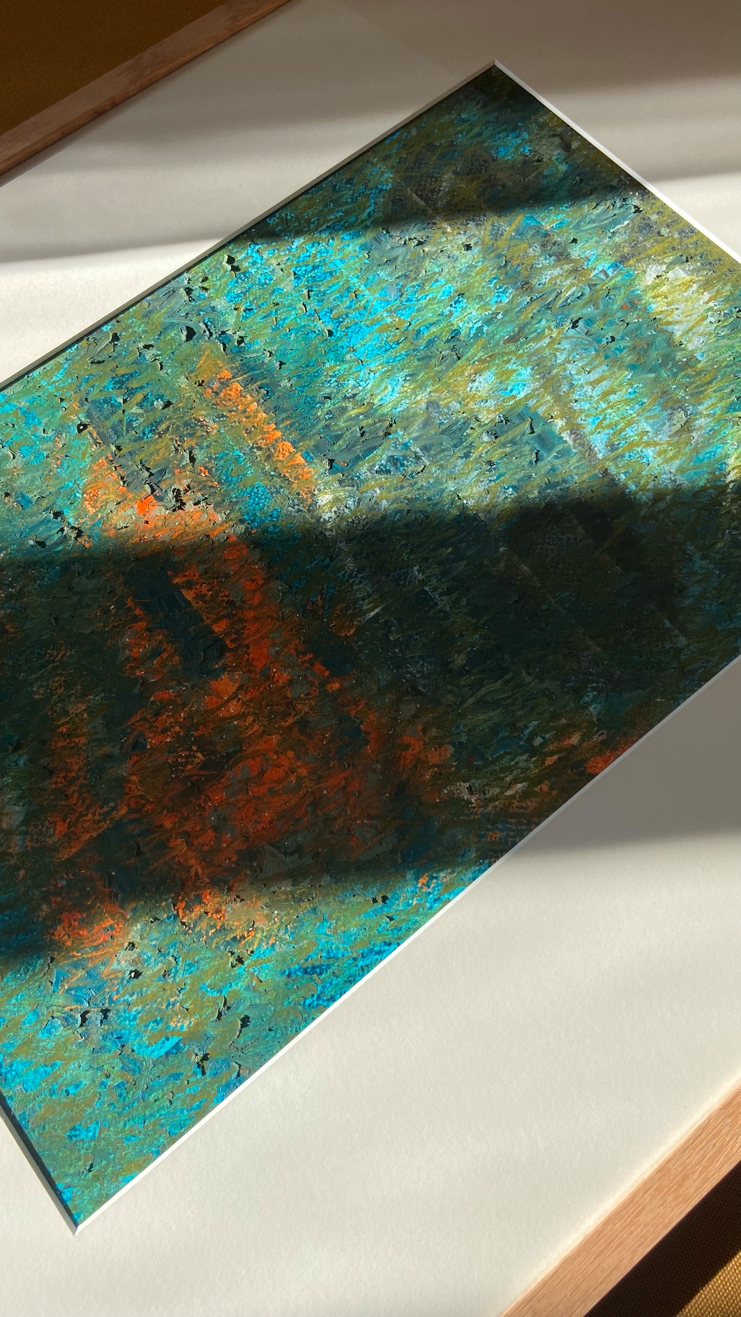 Mehrfarbige Chirografie in Ölpastell und Kreide auf Karton, gerahmt mit Passepartout und Holzrahmen, liegend auf gelbem Polster, partiell mit Sonnenlicht beleuchtet