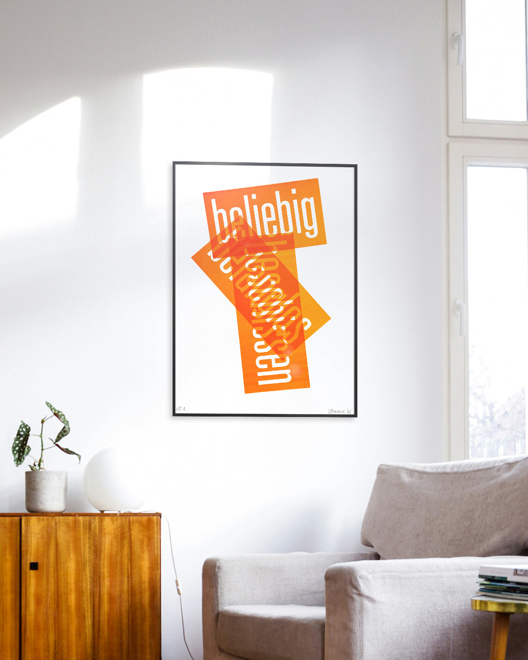 Siebruck mit den Worten »beliebig«, »belanglos« und »beschissen« in Neonorange, gesetzt in schmaler Groteskschrift auf weißem Karton, gerahmt mit schwarzem Rahmen an Zimmerwand, im Vordergrund ein grauer Sessel und eine braune Kommode