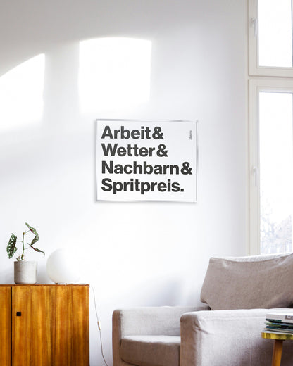 Siebdruck »Arbeit & Wetter & Nachbarn & Spritpreis.« gerahmt als Wandbild in einem modernen Wohnzimmer.