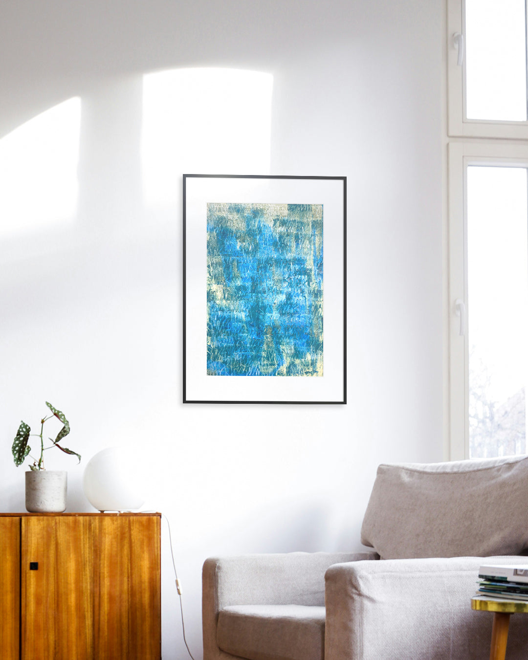 Chirografisches Unikat in Kreide und Ölpastell auf Karton, gerahmt mit schwarzem Rahmen und Passepartout an Zimmerwand, im Vordergrund ein grauer Sessel und eine braune Kommode